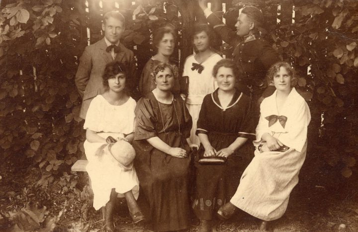 Czarno-białe pozowane zdjęcie grupowe ośmiu osób, w odświętnych strojach w ogrodzie.